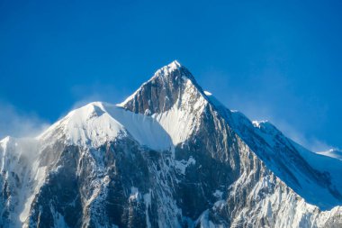Close up view on powder snow covered Himalayas along Annapurna Circuit Trek, Nepal. Harsh and barren landscape around. Clear and blue sky. High Himalayan ranges in the back. Snow capped mountains