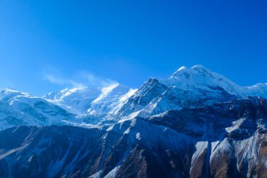 A close up view on Annapurna chain, seen from Manang Valley, Annapurna Circuit Trek in Nepal. Wind blows the snow over the mountain peak. Barren and steep slopes. Harsh landscape. Serenity