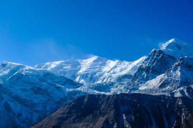 View on high Himalayas along Annapurna Circuit Trek, Nepal. Harsh and barren landscape around. Clear and blue sky. High Himalayan ranges around. Snow capped mountains. Serenity and calmness