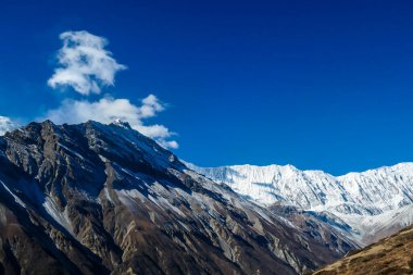 View on high Himalayas along Annapurna Circuit Trek, Nepal. Harsh and barren landscape around. Clear and blue sky. High Himalayan ranges around. Snow capped mountains. Serenity and calmness