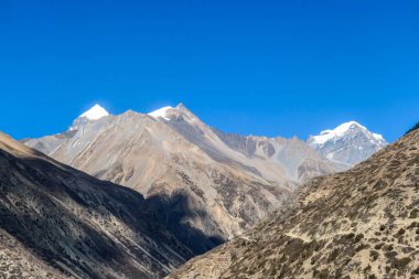 View on high Himalayas along Annapurna Circuit Trek, Nepal. Harsh and barren landscape around. Clear and blue sky. High Himalayan ranges around. Snow capped mountains. Serenity and calmness