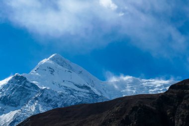View on high Himalayas along Annapurna Circuit Trek, Nepal. Harsh and barren landscape around. Clear and blue sky. High Himalayan ranges around. Snow capped mountains. Serenity and calmness