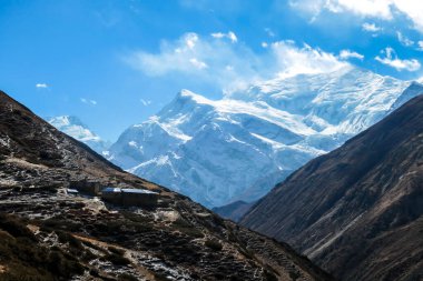 A small cottage located on steep slopes of Manang Valley, Annapurna Circus, Himalayas, Nepal, with Annapurna Chain and Gangapurna in the back. Dry and desolated landscape. Snow capped mountains
