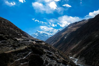 A small cottage located on steep slopes of Manang Valley, Annapurna Circus, Himalayas, Nepal, with Annapurna Chain and Gangapurna in the back. Dry and desolated landscape. Snow capped mountains