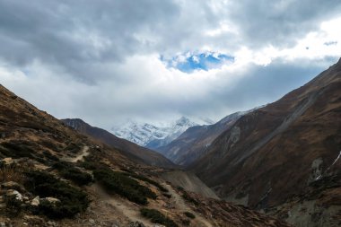 Harsh and golden colored slopes in Manang Valley, Annapurna Circus Trek, Himalayas, Nepal, with the view on Annapurna Chain and Gangapurna. Dry and desolated landscape. High snow capped mountain peaks