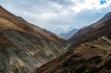 Harsh and golden colored slopes in Manang Valley, Annapurna Circus Trek, Himalayas, Nepal, with the view on Annapurna Chain and Gangapurna. Dry and desolated landscape. High snow capped mountain peaks