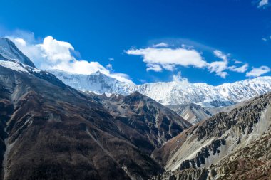 A panoramic view on a valley along Annapurna Circuit in Nepal. In the back there are high, snow capped Himalayan peaks. Slopes are overgrown with small bushes. Exploration and discovering