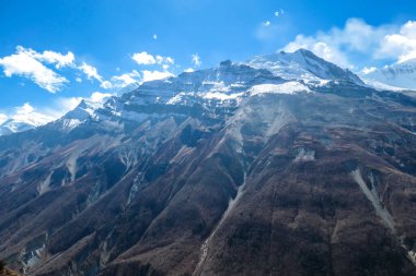 A panoramic view on sharp and dangerous, high, snow capped Himalayan peaks long Annapurna Circuit in Nepal. Slopes are overgrown with small bushes. Exploration and discovering. Steep mountain wall.