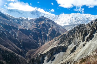 A panoramic view on a valley along Annapurna Circuit in Nepal. In the back there are high, snow capped Himalayan peaks. Slopes are overgrown with small bushes. Exploration and discovering