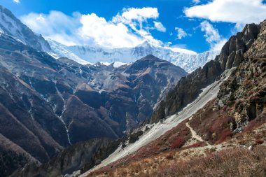 A panoramic view on a valley along Annapurna Circuit in Nepal. In the back there are high, snow capped Himalayan peaks. Slopes are overgrown with small bushes. Exploration and discovering