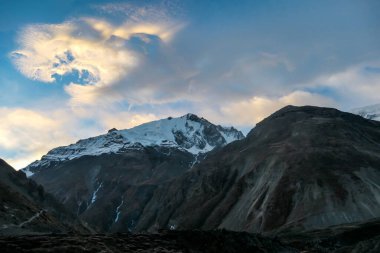 A close up view on high, snow capped Himalayan peaks along Annapurna Circuit in Nepal. Barren and sharp slopes. Mountains are partially shrouded with clouds. Exploration and discovering new places
