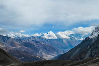 A panoramic view on high, snow capped Himalayan peaks along Annapurna Circuit in Nepal. Barren and sharp slopes. Mountains are partially shrouded with clouds. Exploration and discovering new places