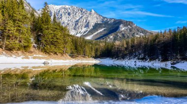 Winter landscape of Austrian Alps with Green Lake in the middle. Powder snow covering the mountains and ground. Emerald color of water. Soft reflection of Alps in calm lake's water. Winter wonderland