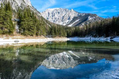 Winter landscape of Austrian Alps with Green Lake in the middle. Powder snow covering the mountains and ground. Soft reflections of Alps in calm lake's water. Winter wonderland. Serenity and calmness