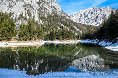 Winter landscape of Austrian Alps with Green Lake in the middle. Powder snow covering the mountains and ground. Soft reflections of Alps in calm lake's water. Winter wonderland. Serenity and calmness