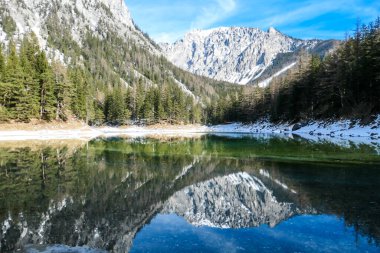 Winter landscape of Austrian Alps with Green Lake in the middle. Powder snow covering the mountains and ground. Soft reflections of Alps in calm lake's water. Winter wonderland. Serenity and calmness