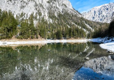 Winter landscape of Austrian Alps with Green Lake in the middle. Powder snow covering the mountains and ground. Soft reflections of Alps in calm lake's water. Winter wonderland. Serenity and calmness