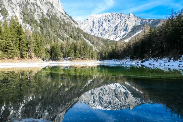 Winter landscape of Austrian Alps with Green Lake in the middle. Powder snow covering the mountains and ground. Soft reflections of Alps in calm lake\'s water. Winter wonderland. Serenity and calmness