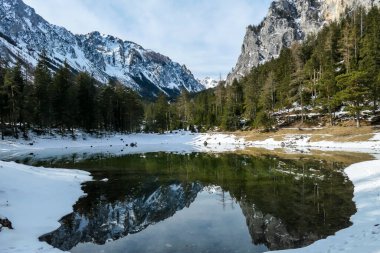 Winter landscape of Austrian Alps with Green Lake in the middle. Powder snow covering the mountains and ground. Soft reflections of Alps in calm lake's water. Winter wonderland. Serenity and calmness