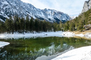 Winter landscape of Austrian Alps with Green Lake in the middle. Powder snow covering the mountains and ground. Soft reflections of Alps in calm lake's water. Winter wonderland. Serenity and calmness