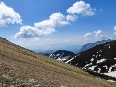 A panoramic view on a massive, stony mountains in Hochturm region, Austrian Alps. There are endless mountains chains in the back. The slopes are overgrown with moss and grass. Sunny and bright day.
