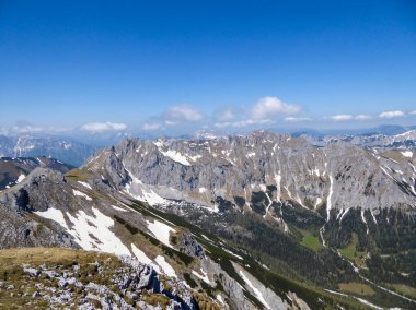 A panoramic view on a massive, stony mountains in Hochturm region, Austrian Alps. There are endless mountains chains in the back. The slopes are overgrown with moss and grass. Sunny and bright day.