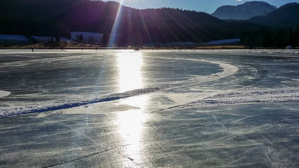 An ice rink on frozen Weissensee lake in Austria. The lake is surrounded by mountains. The ice rink is well prepared. Winter activity on a clear and bright day. Winter wonderland. Happiness