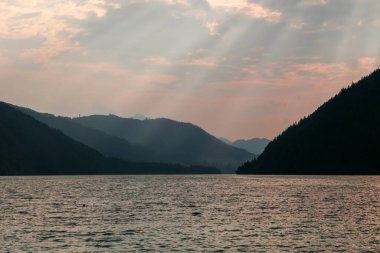 An early morning at the Weissensee lake in Austria. The sky is bursting with orange. The lake is surrounded by high Alps. Endless chains of mountains. Serenity and peacefulness. Day break