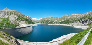 A Koelnbreinsperre dam in Austria. The dam is build in high Alps. The lake stretches over a vast territory. The dam is surrounded by mountains. In the back there is a glacier. Controlling the nature