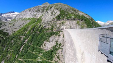 A Koelnbreinsperre dam in Austria. The dam is build in high Alps. The lake stretches over a vast territory. The dam is surrounded by mountains. In the back there is a glacier. Controlling the nature
