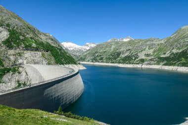 A Koelnbreinsperre dam in Austria. The dam is build in high Alps. The lake stretches over a vast territory. The dam is surrounded by mountains. In the back there is a glacier. Controlling the nature