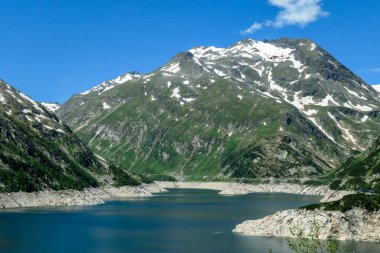 Dam in Austrian Alps. The artificial lake stretches over a vast territory, shining with navy blue color. The dam is surrounded by high mountains. In the back there is a glacier. Controlling the nature