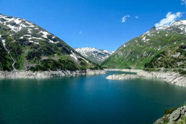 Dam in Austrian Alps. The artificial lake stretches over a vast territory, shining with navy blue color. The dam is surrounded by high mountains. In the back there is a glacier. Controlling the nature