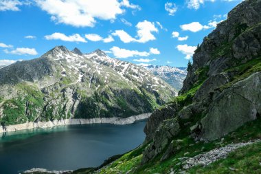 Dam in Austrian Alps. The artificial lake stretches over a vast territory, shining with navy blue color. The dam is surrounded by high mountains. In the back there is a glacier. Controlling the nature