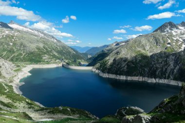 Dam in Austrian Alps. The artificial lake stretches over a vast territory, shining with navy blue color. The dam is surrounded by high mountains. In the back there is a glacier. Controlling the nature