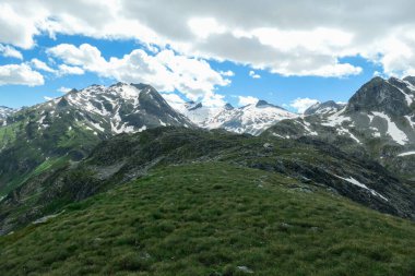 Panoramic view on huge glacier in Maltal region in Austrian Alps. The valley below it flourishing with green and freshness., small torrent in the middle. Summer in the mountains. Serenity and solitude