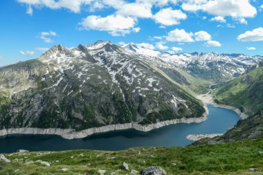 Dam in Austrian Alps. The artificial lake stretches over a vast territory, shining with navy blue color. The dam is surrounded by high mountains. In the back there is a glacier. Controlling the nature clipart