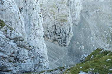 A top down view on the narrow trail along lose stones. There are sharp mountains and high peaks around. Dangerous mountain climbing. Bright day. Serenity and freedom.