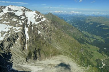 Panoramic view from top of Hohe Sonnblick in Austrian Alps on Grossglockner. The whole area is partially covered with snow, lush green meadows below. Many mountain chains in the back. Sunny day.