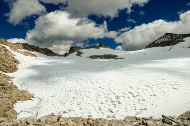 A footprints on the snow, lying on a glacier under Hohe Sonnblick in Austrian Alps. The footprints lead in one direction. Many high mountain peaks. Clear and sunny day. Creeks on the glacier