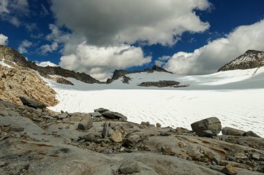 A footprints on the snow, lying on a glacier under Hohe Sonnblick in Austrian Alps. The footprints lead in one direction. Many high mountain peaks. Clear and sunny day. Creeks on the glacier