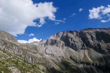 A view on steep and high mountain chain in Heiligenblut region, Austria. There are few small waterfall along the slopes. The slopes are overgrown with moss and grass. High Alpine landscape