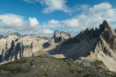 A capture of high and sharp peaks of Dolomites in Italy. Dried grass on the meadow. The sky is full of soft clouds. Lots of lose stones and pebbles. Raw and desolated landscape. Serenity and calmness