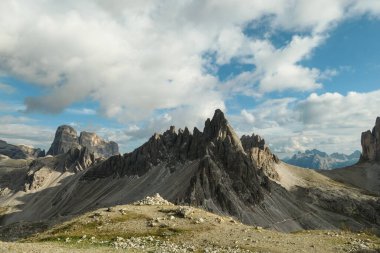 A capture of high and sharp peaks of Dolomites in Italy. Dried grass on the meadow. The sky is full of soft clouds. Lots of lose stones and pebbles. Raw and desolated landscape. Serenity and calmness