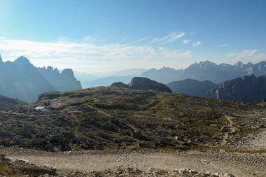 A view on a vast valley in Italian Dolomites. The valley is surrounded with high mountains from each side. Strong, early morning sun. There are a few clouds above. Remote and isolated place. Remedy