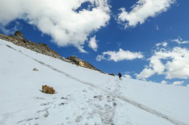 A woman following the narrow footprints path while crossing the glacier under Hohe Sonnblick in Austrian Alps. The footprints lead in one direction. Many high mountain chains in the nearby. Sunny day