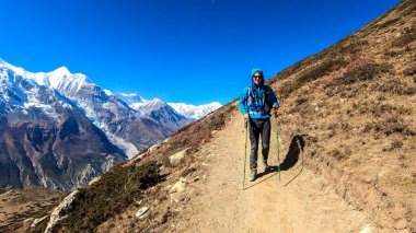 A man trekking on the Annapurna Circuit Trek, Himalayas, Nepal. Panoramic view on snow caped Annapurna chain. Lots of dried grass. High altitude, massive mountains. Freedom and adventure