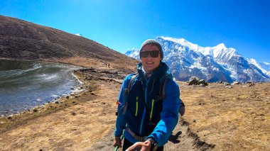 A man trekking along the Ice Lake, Annapurna Circuit Trek detour, Himalayas, Nepal, surrounded by high, snow caped mountains. Annapurna Chain in the back. High altitude lake. Harsh landscape.