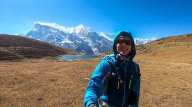 Man taking a selfie while trekking along the Ice Lake, Annapurna Circuit Trek detour, Himalayas, Nepal, surrounded by high, snow caped Annapurna chain in the back. High altitude lake. Harsh landscape