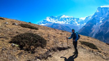 A man trekking on the Annapurna Circuit Trek, Himalayas, Nepal. Panoramic view on snow caped Annapurna chain. Lots of dried grass. High altitude, massive mountains. Freedom and adventure